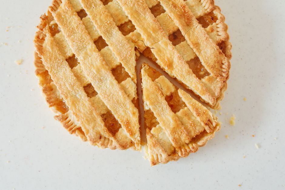 Top view of a freshly baked sliced apple pie with lattice crust on a white background.